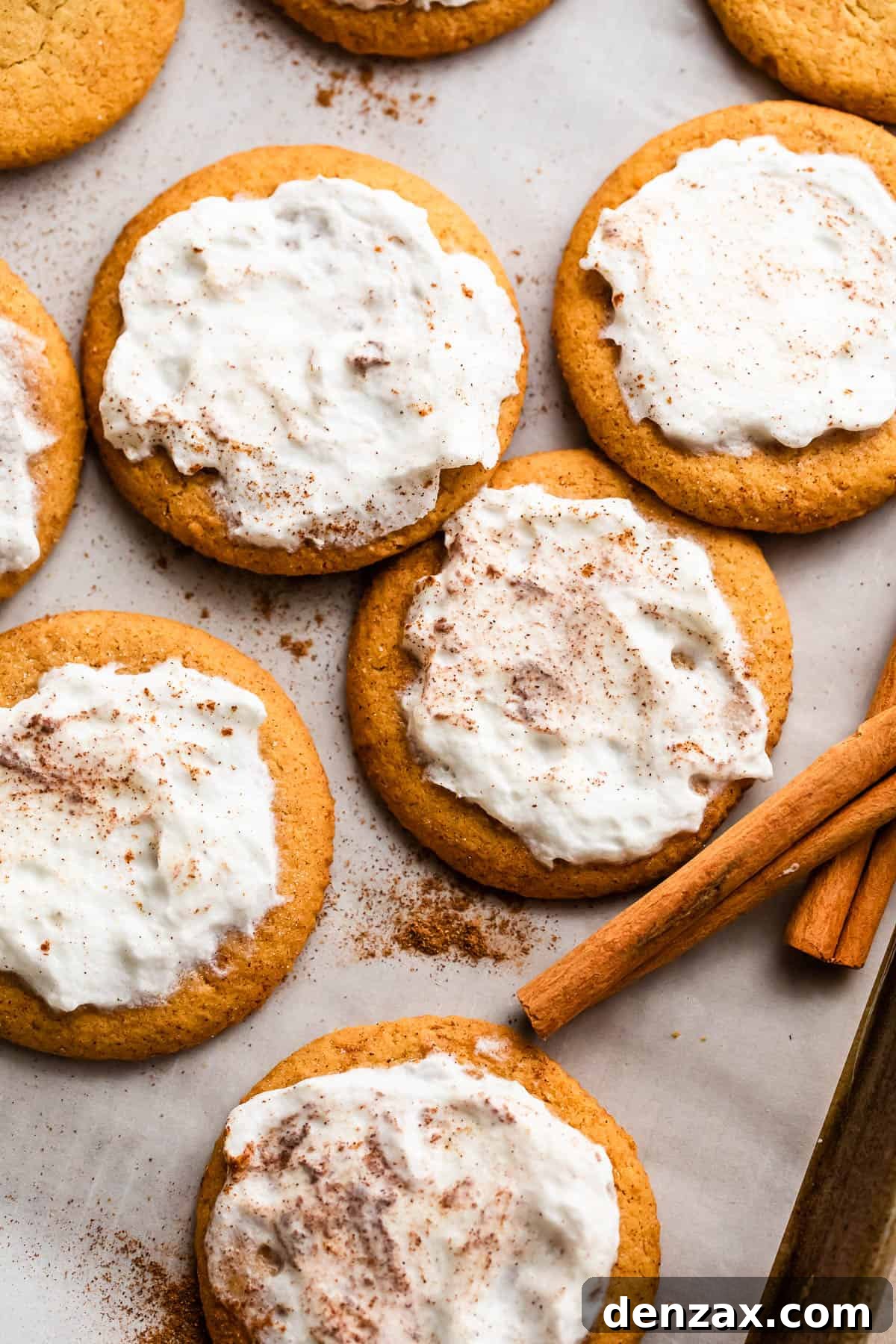 Overhead shot of soft pumpkin cookies generously topped with homemade cream cheese frosting and a sprinkle of cinnamon, arranged on a parchment-lined baking sheet, inviting you to indulge in their seasonal charm.