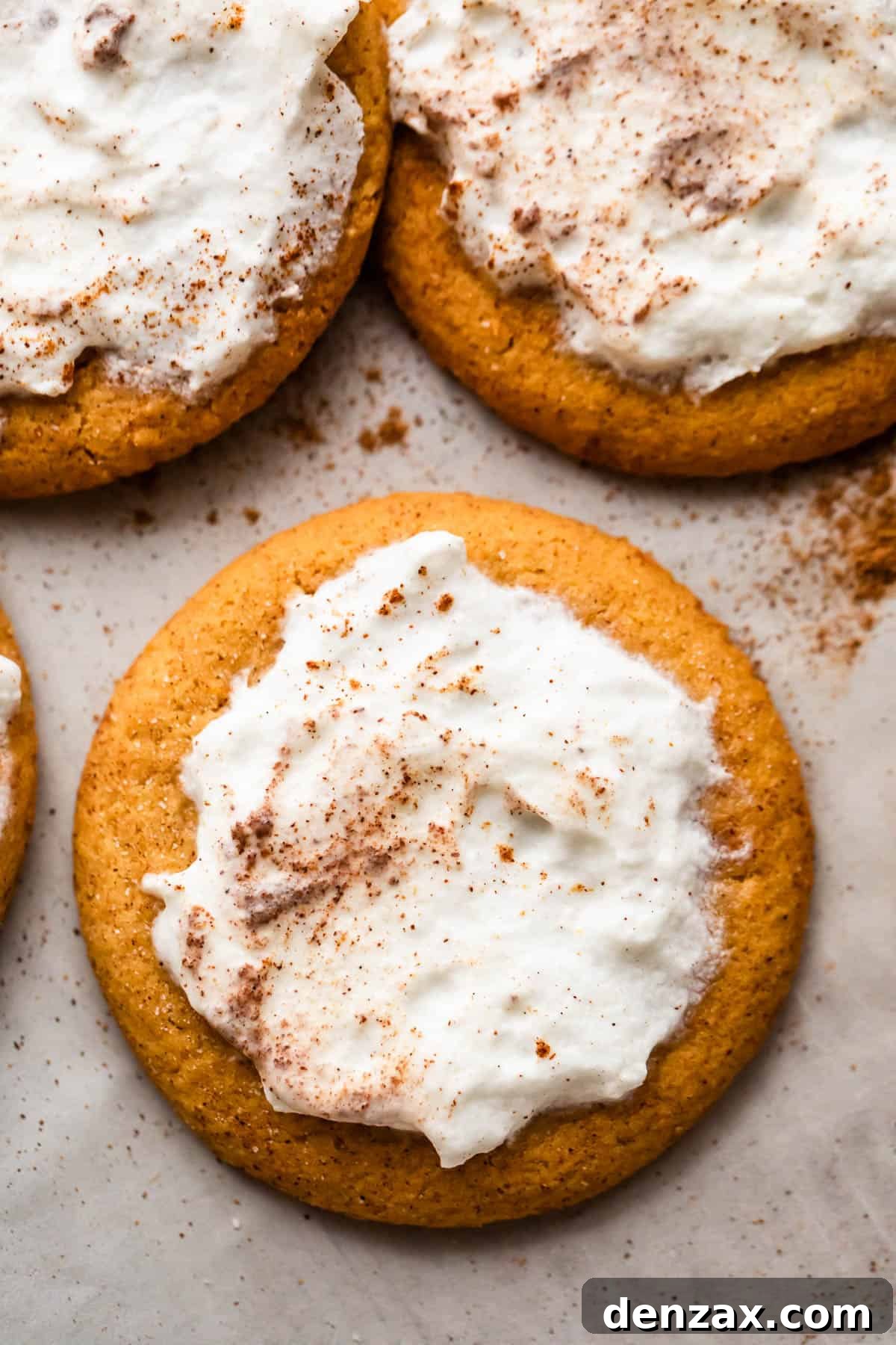 Three beautifully frosted pumpkin cookies showcasing their soft, cake-like texture and creamy topping, presented for a delightful treat, inviting you to take a bite.