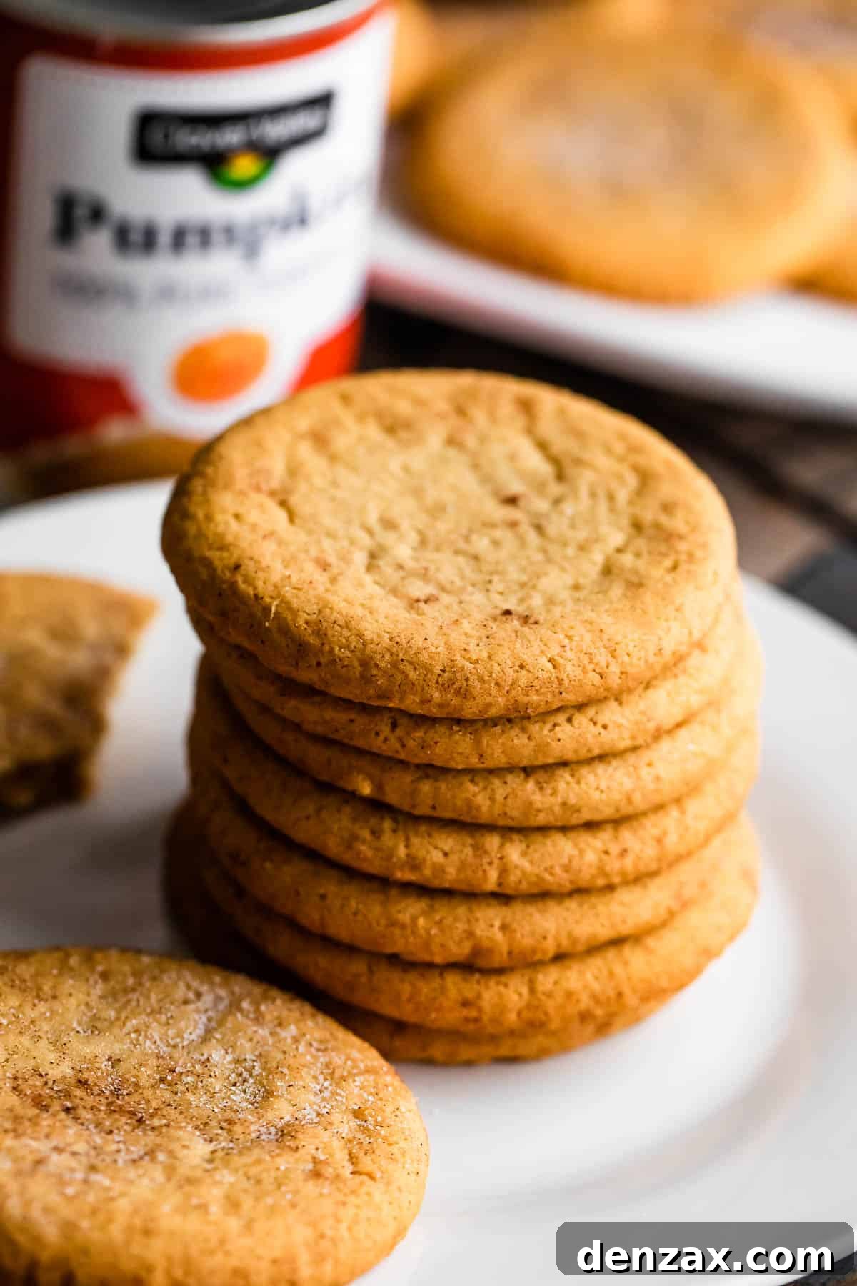 A warm stack of homemade pumpkin cookies, delicately frosted, rests on a white plate with a can of pumpkin puree in the background, signaling the seasonal delight and inviting comfort.