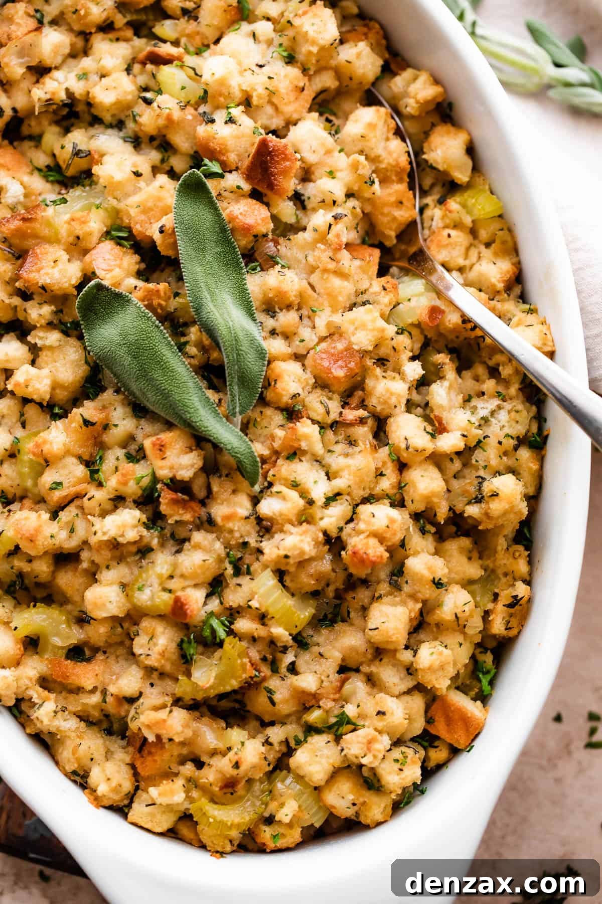 Freshly baked herb stuffing, beautifully golden brown and sprinkled with vibrant sage leaves and other minced herbs, presented in an elegant white ceramic dish.