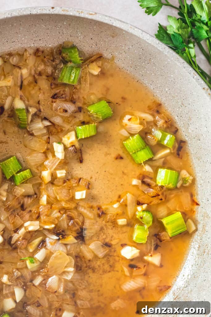 A close-up view of a ceramic skillet containing a sautéed mixture of chopped onions, celery, and garlic, deglazed with white wine, creating a fragrant base for the stuffing.