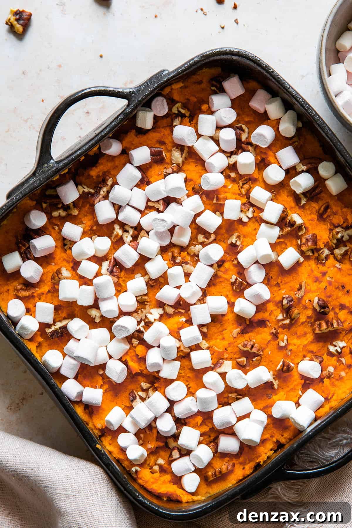 A close-up shot of the unbaked sweet potato casserole, revealing the smooth sweet potato base generously sprinkled with chopped pecans and mini marshmallows, ready for the oven.