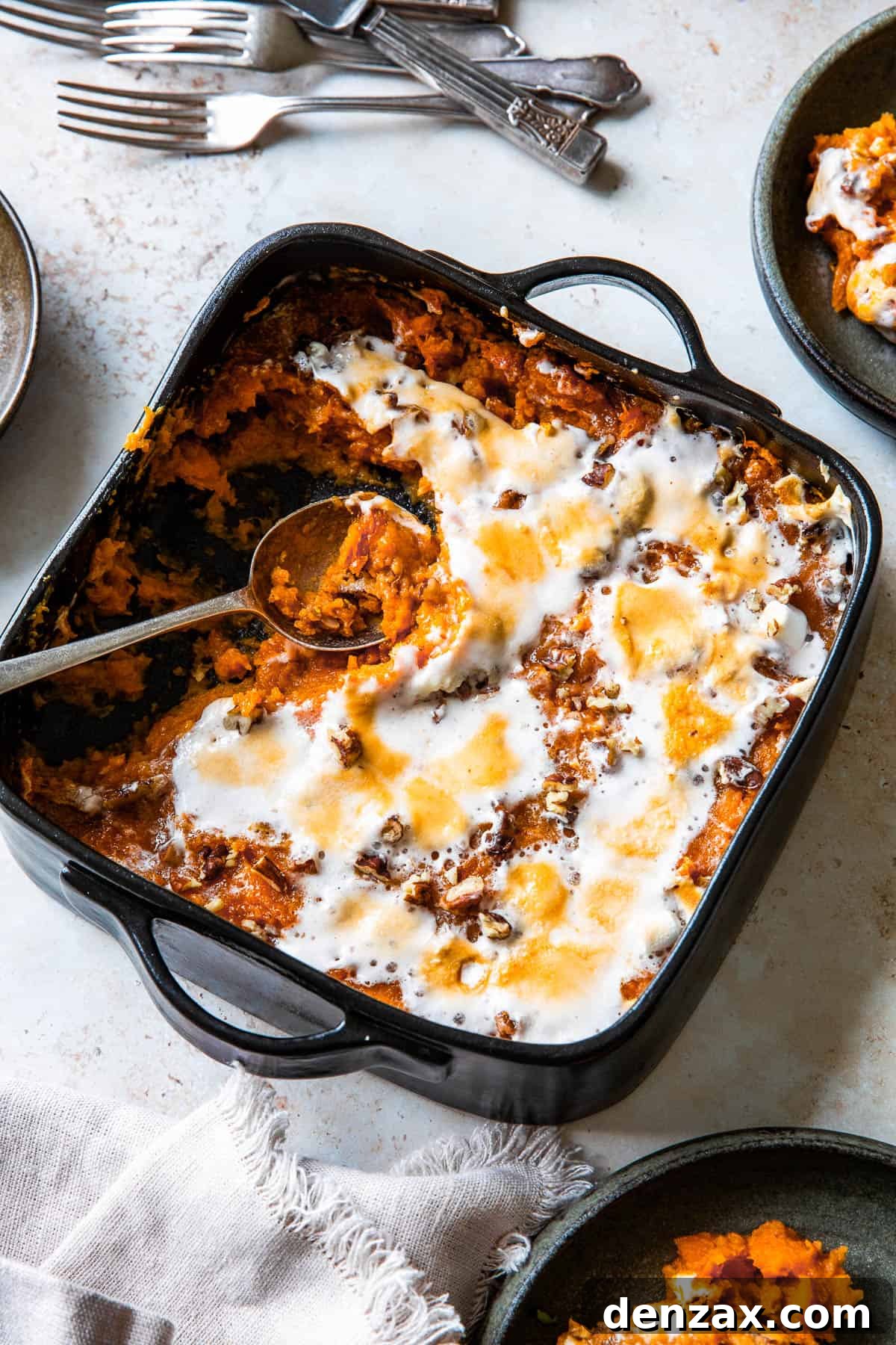 A square black baking dish filled with perfectly baked sweet potato casserole, featuring a glistening, golden-brown melted marshmallow topping. Several portions have been scooped out, revealing the creamy sweet potato interior.