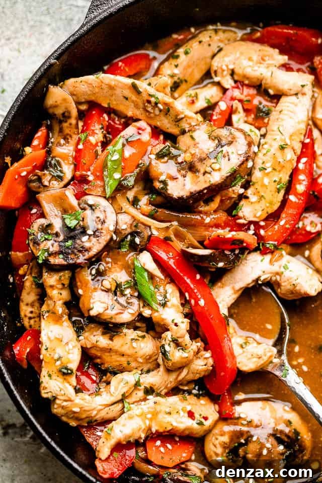 A large skillet full of freshly cooked chicken stir fry, beautifully garnished with green onions and sesame seeds, ready to be served.
