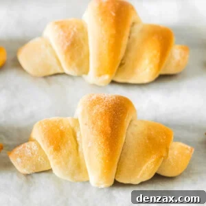 A row of crescent rolls on a parchment-lined baking sheet, golden brown and ready to be served.