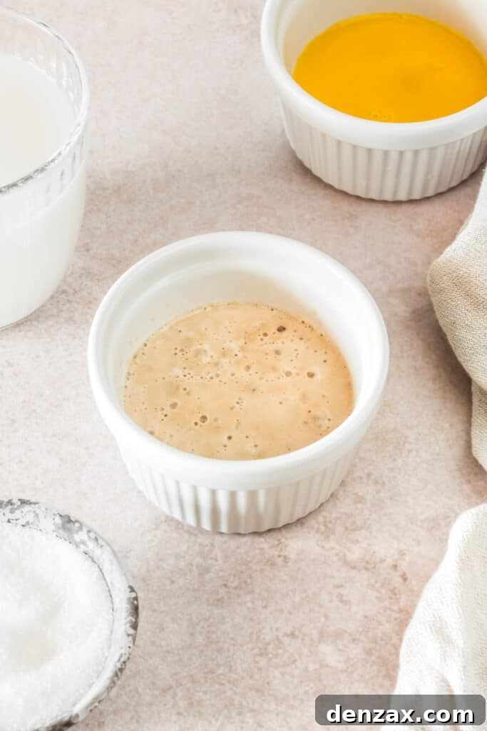 Yeast and warm water beginning to bubble in a small ramekin, indicating activation.