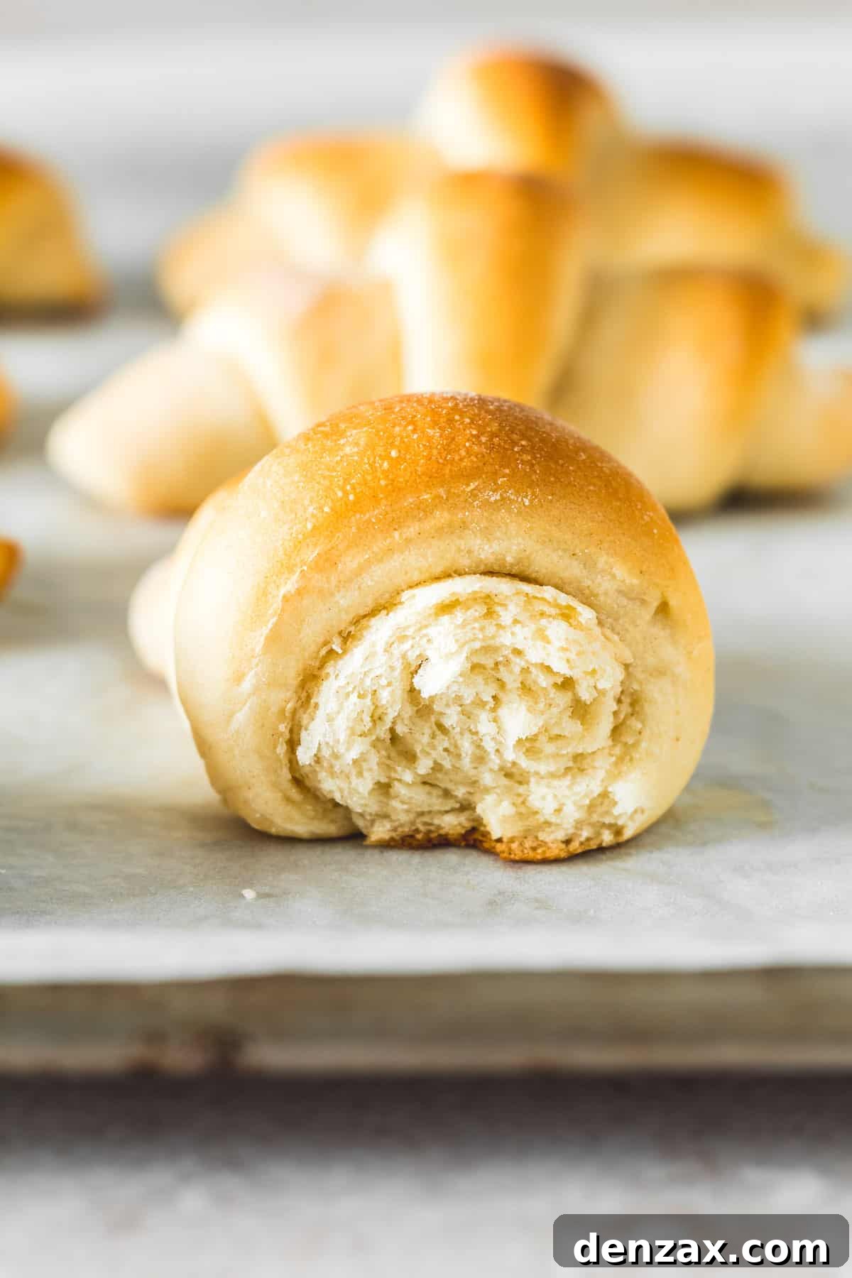 A side view of one crescent roll with an end gently broken off, revealing its soft, airy texture and delicate layers.