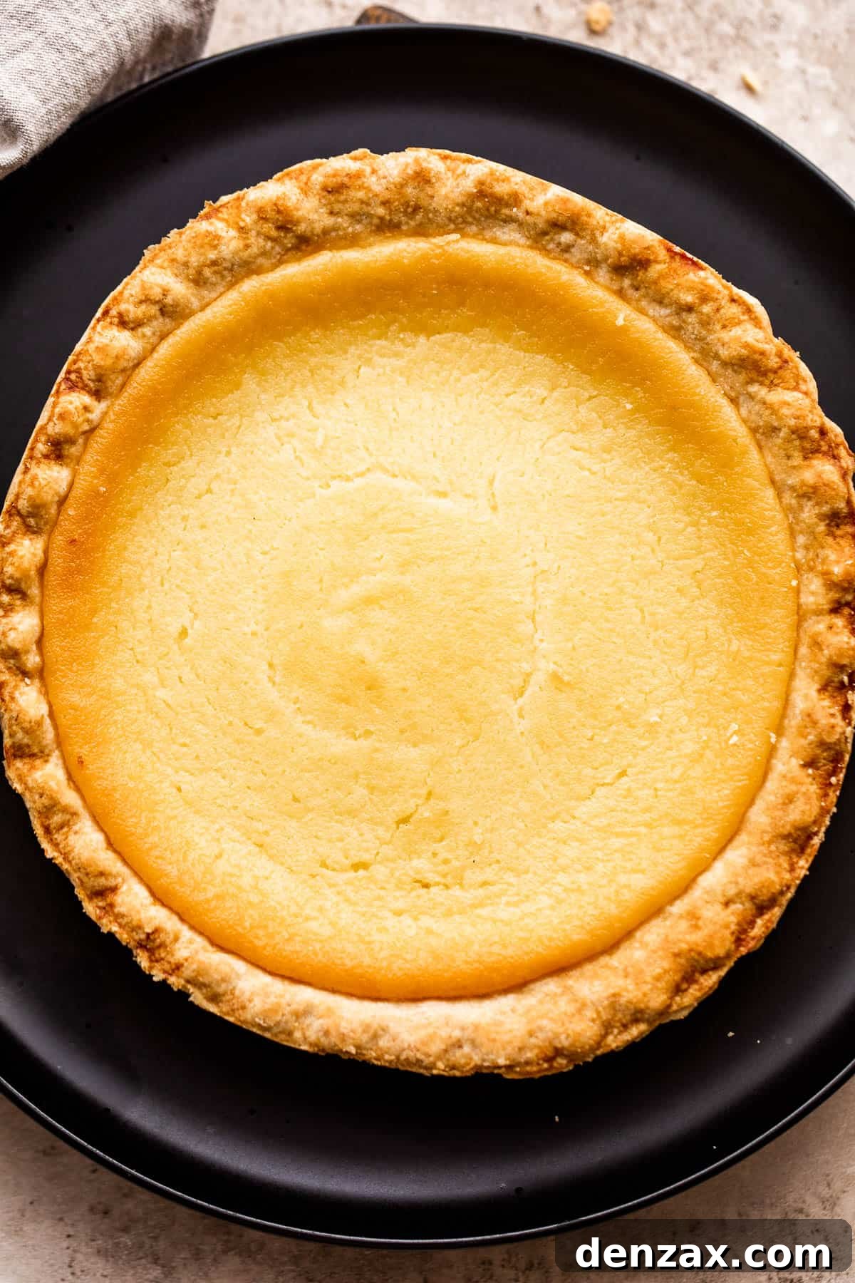 An overhead shot capturing a perfectly baked homemade Southern Buttermilk Pie, presented elegantly on a minimalist black plate, ready to be served.