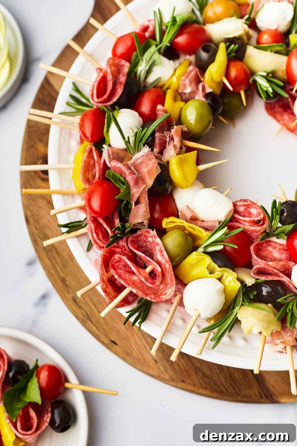 A detailed close-up of a Holiday Antipasto Wreath, highlighting the intricate arrangement of skewers laden with prosciutto, tangy pepperoncini, sweet grape tomatoes, fresh mozzarella, and aromatic basil leaves.