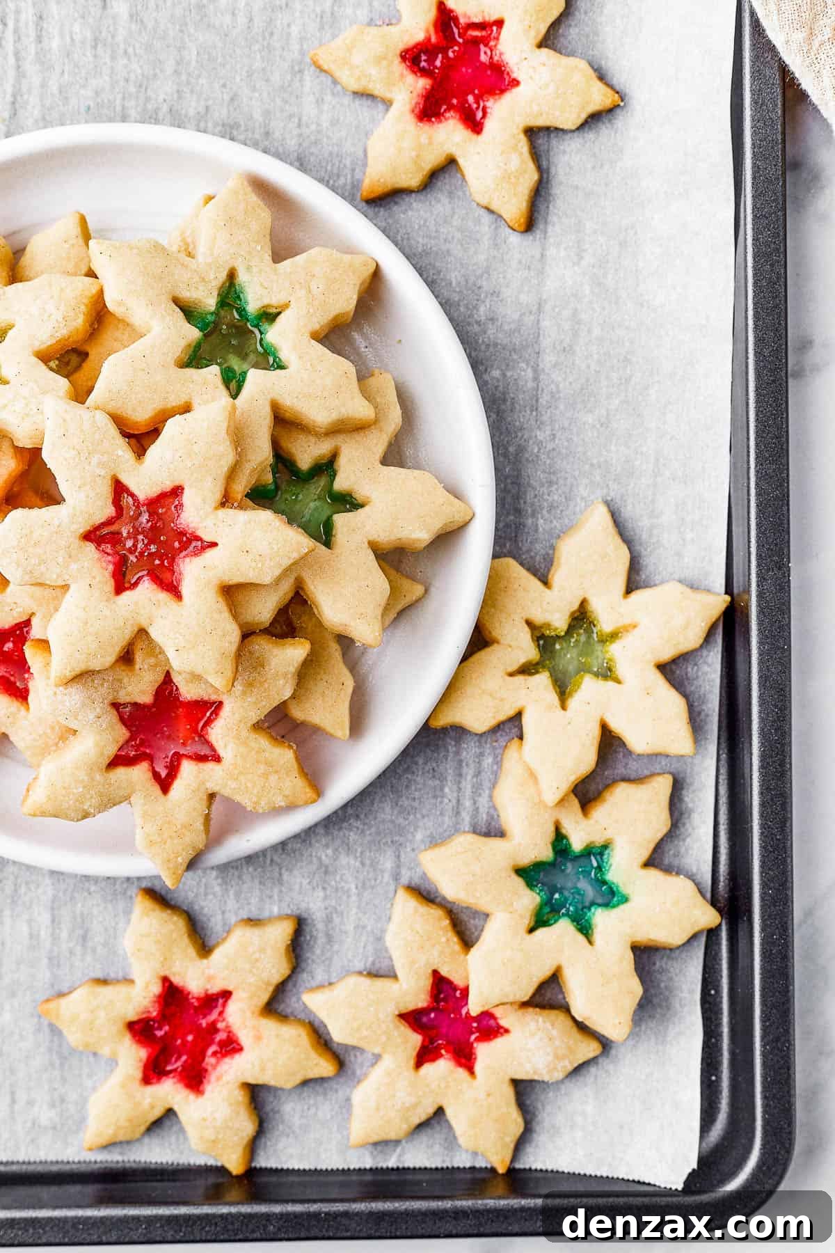 Two plates of stained glass cookies, with extra cookies arranged artistically on the table, along with a glass of milk.