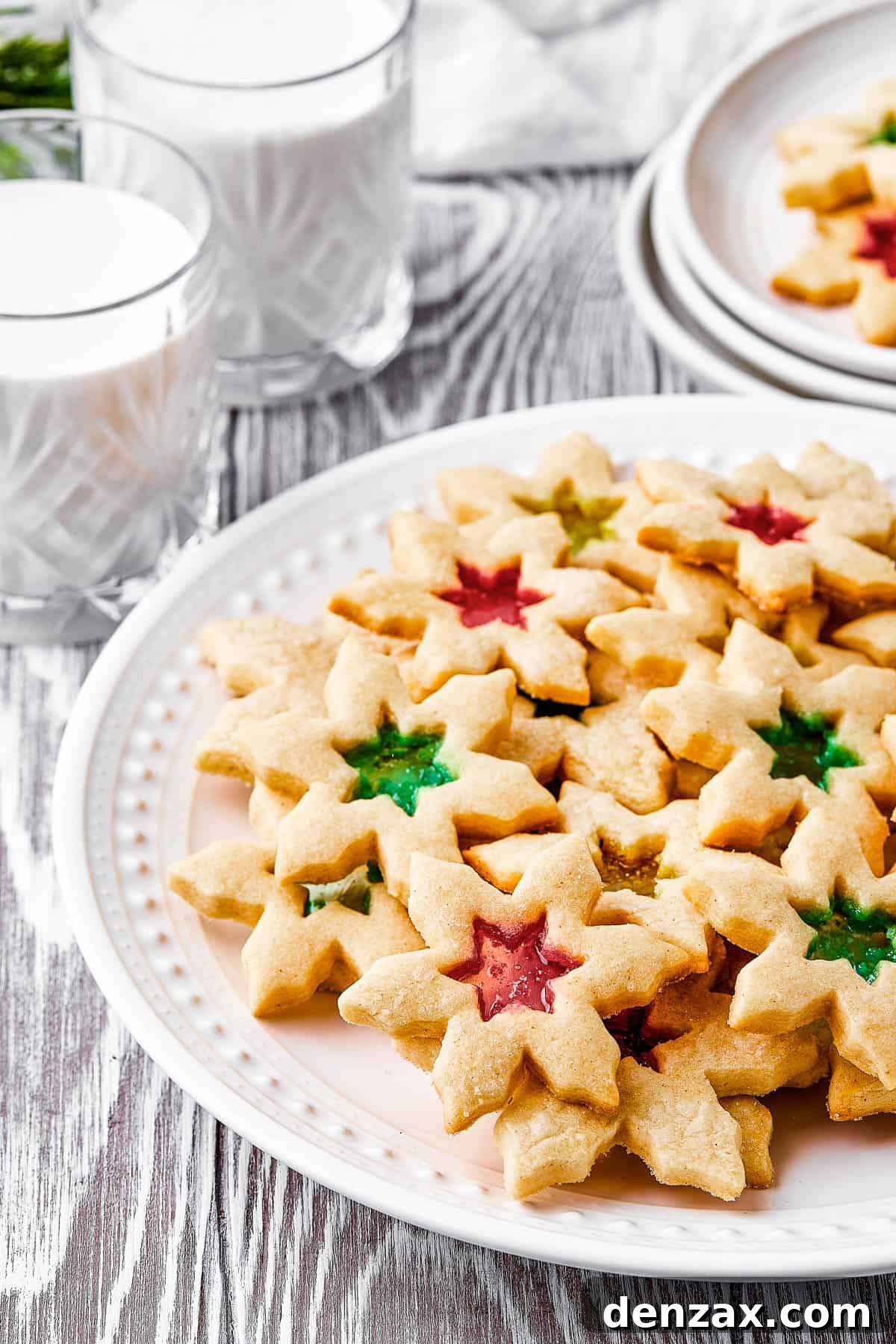 A platter of cookies with glasses of milk arranged around it. Two cookies are on a small serving plate.