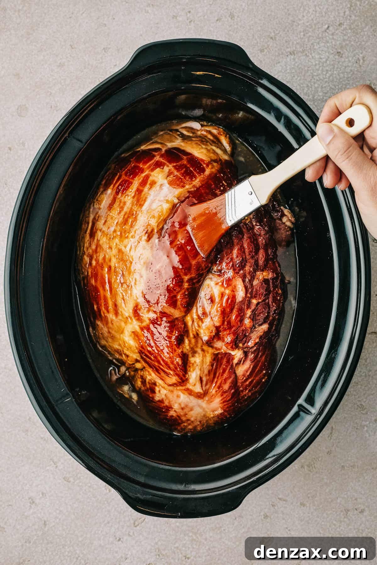 Overhead shot of a ham in a crockpot insert, being brushed with glaze.