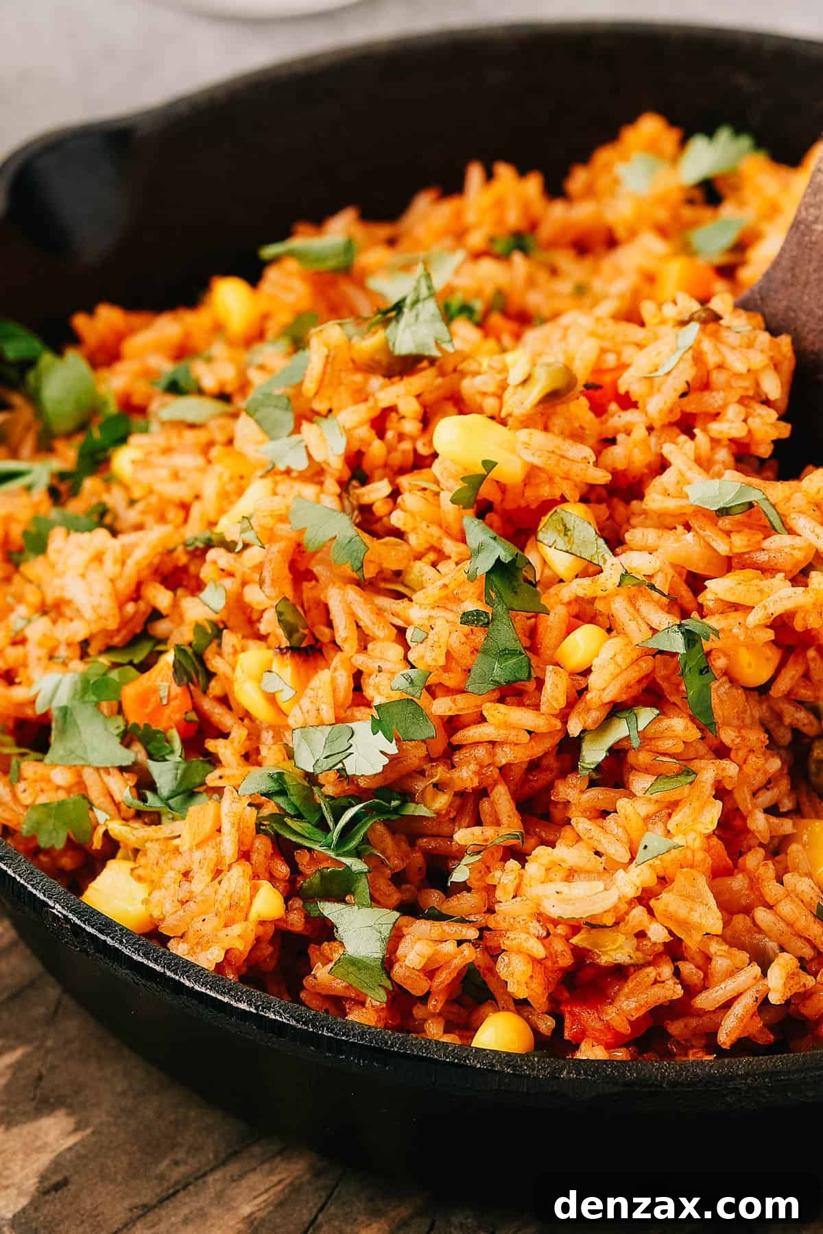 Instant Pot Fiesta Rice 3 Side view of Mexican rice in a cast iron skillet, with a wooden utensil in the pan.