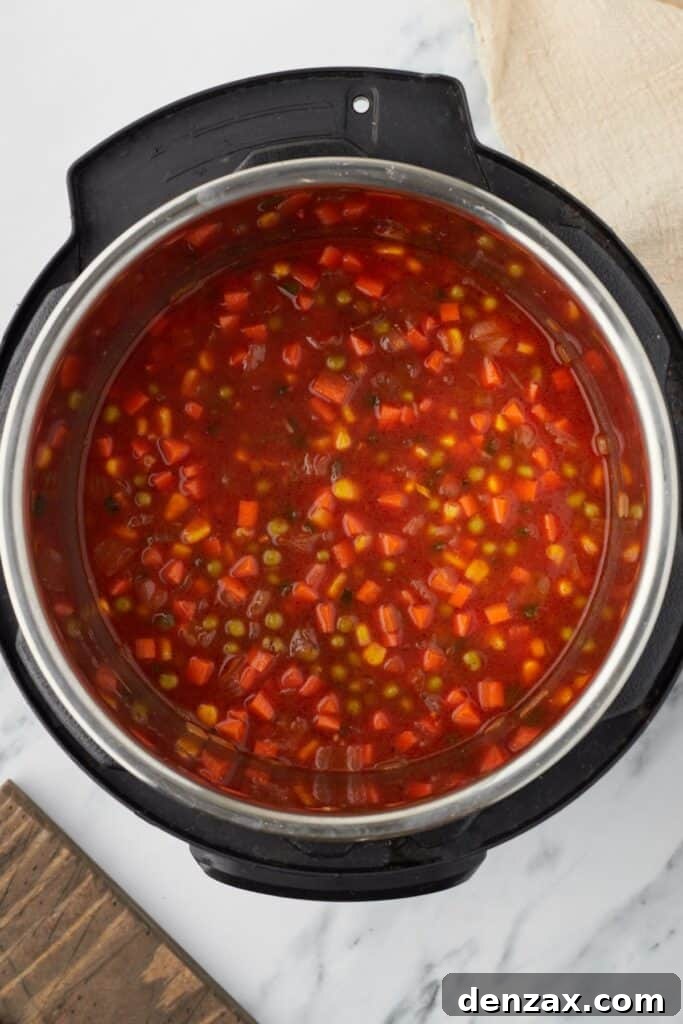 Instant Pot Fiesta Rice 7 Overhead shot of an Instant Pot, with vegetables and a tomato-based broth inside.