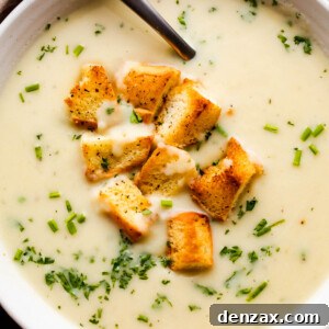 overhead close up shot of leek and potato soup served in a white bowl and garnished with croutons and chopped chives.