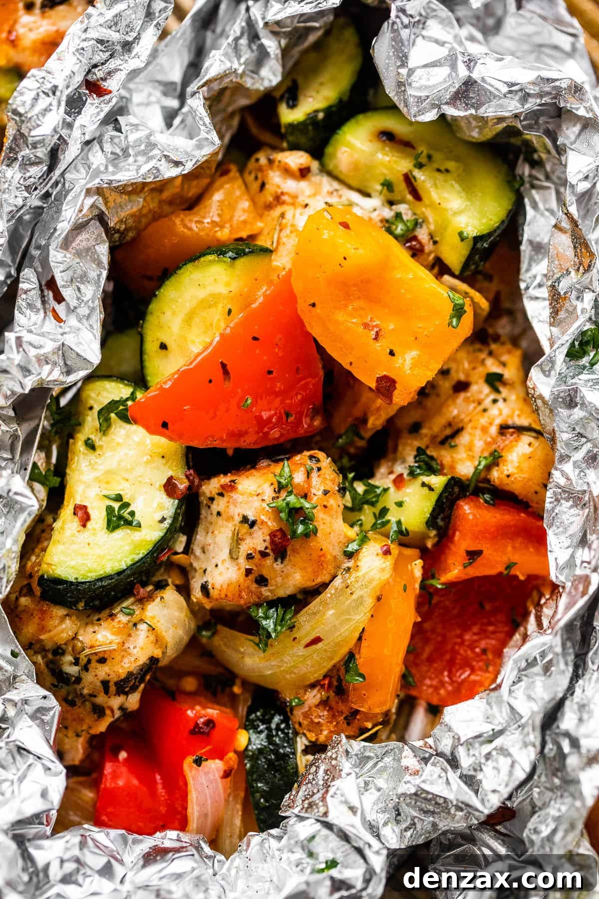 Up close shot of diced chicken, sliced zucchini, and sliced peppers all layered in an aluminum foil packet, ready for cooking.