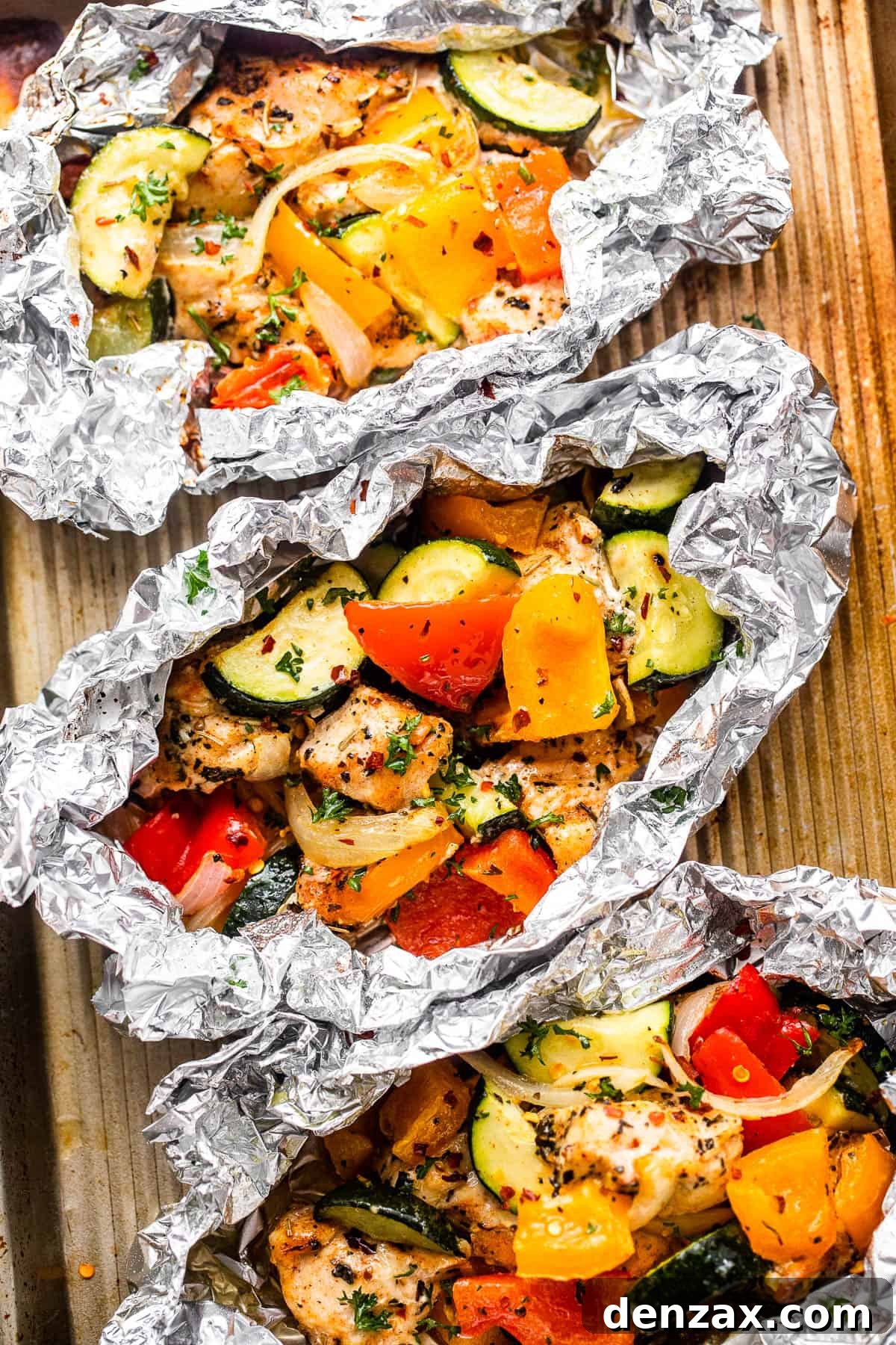 Overhead shot of diced chicken, sliced zucchini, and sliced peppers all layered in an aluminum foil packet, showcasing the colorful ingredients.