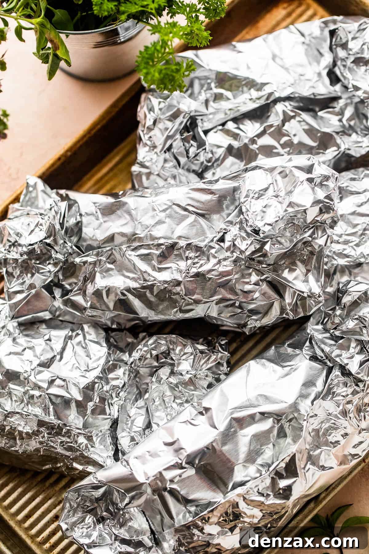 Several sealed foil packets arranged neatly on a baking sheet, ready for the oven.