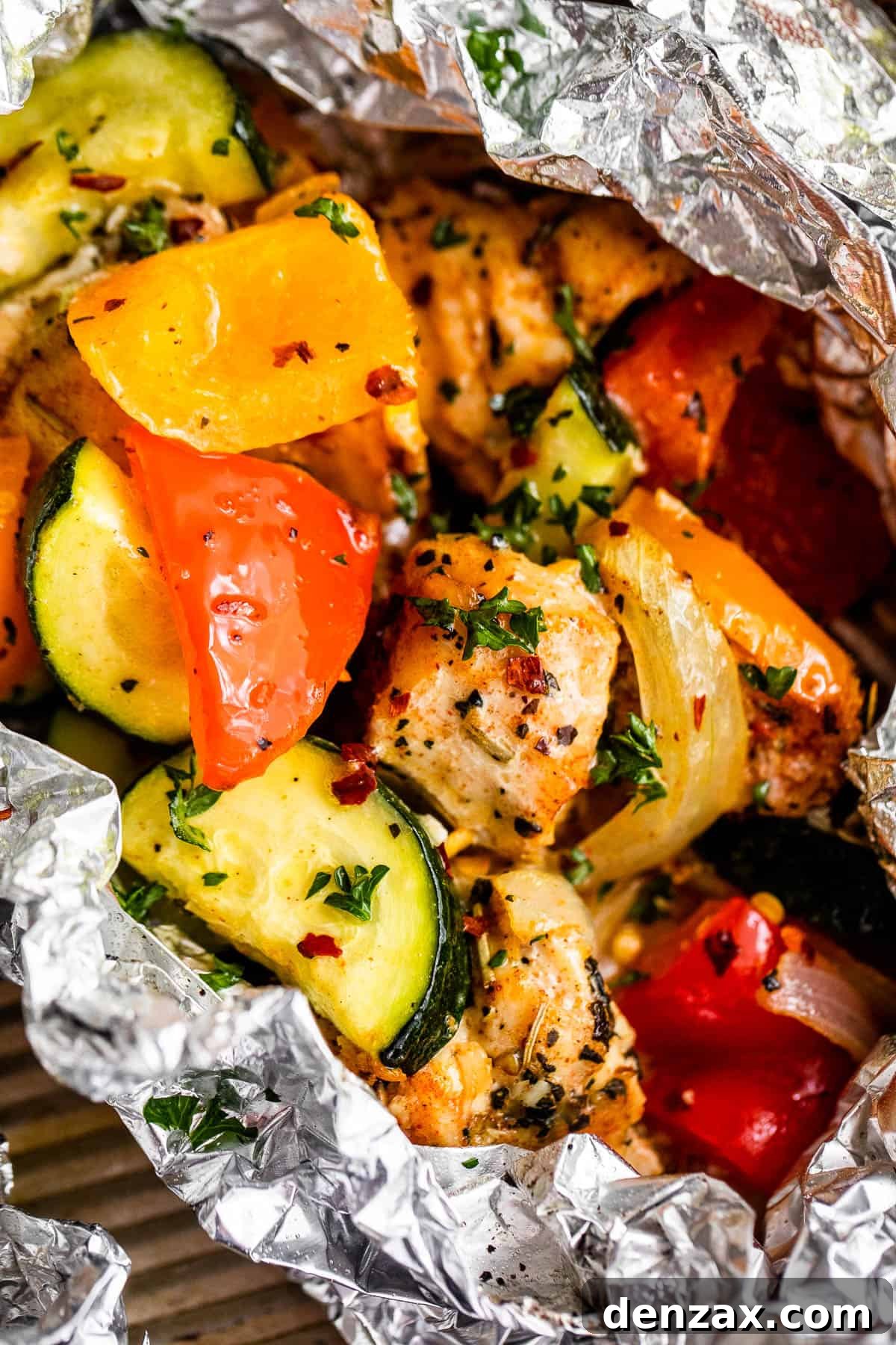 Up close shot of diced chicken, sliced zucchini, and sliced peppers all layered in an aluminum foil packet, glistening with seasoning.