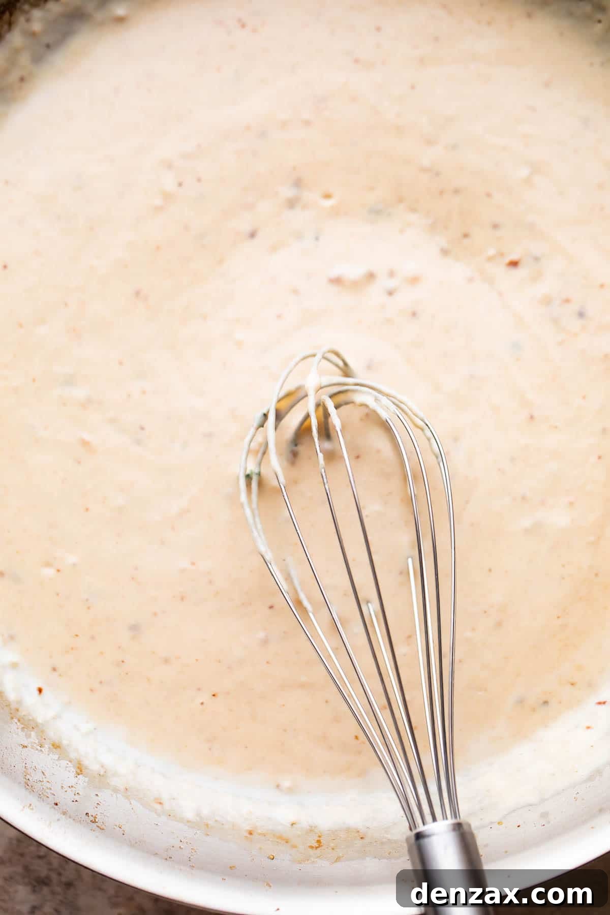 whisking through white cream sauce in a skillet.