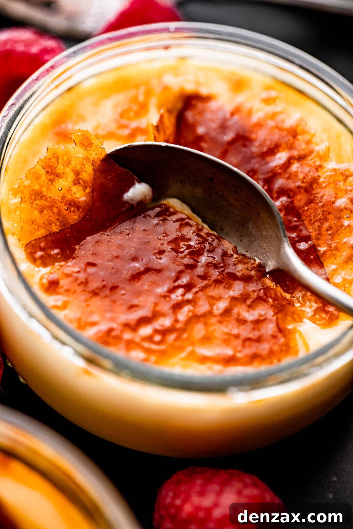 Close-up side shot of a spoon breaking through the perfectly burnt sugar top of a Creme Brulee, revealing the smooth custard beneath.