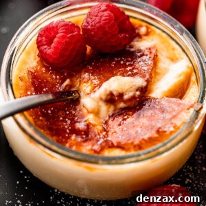 Side shot of Creme Brulee in a glass jar, topped with two raspberries, and a spoon inside the jar.