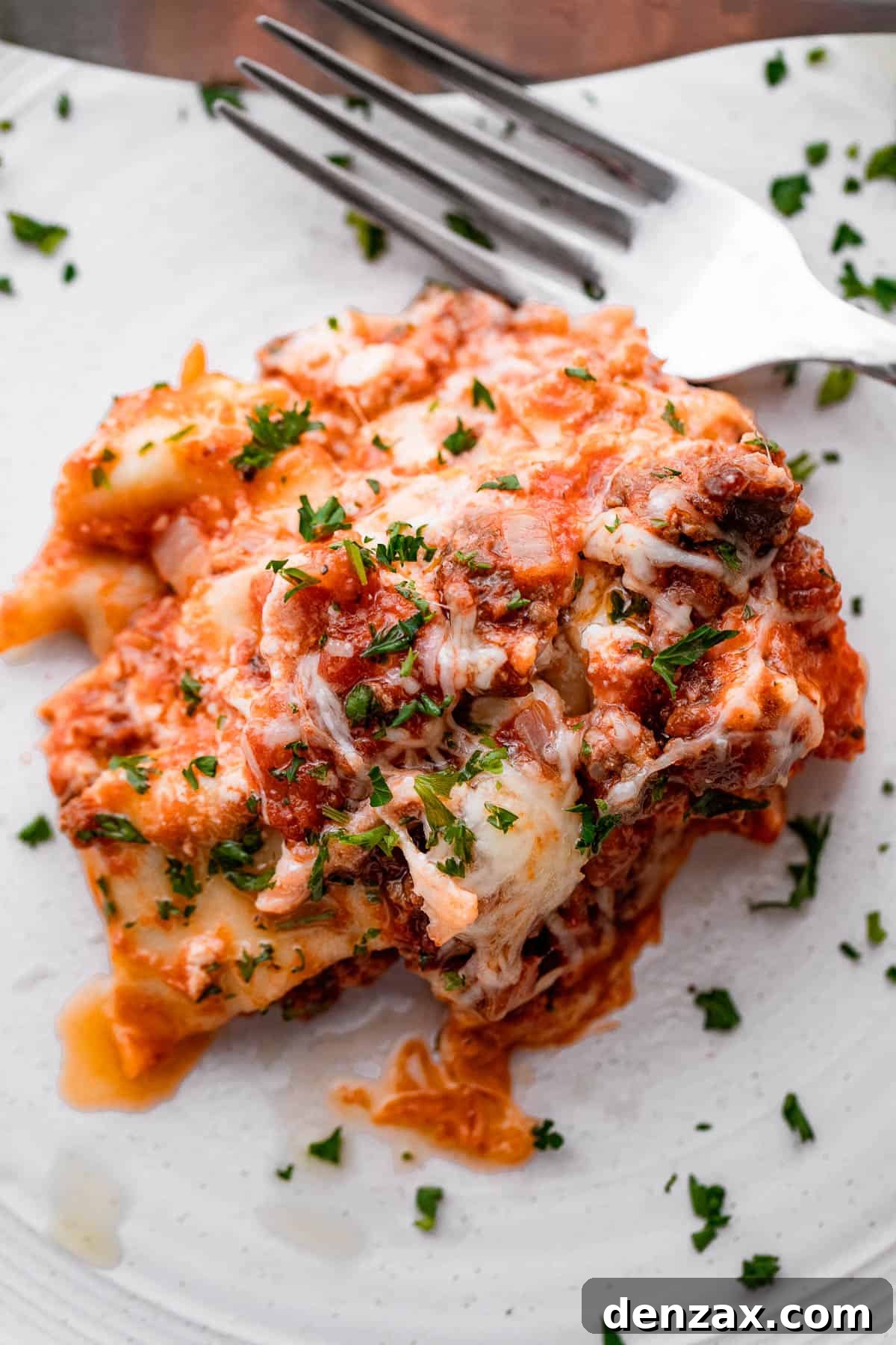 piece of lasagna served on a white plate with a fork placed to the side of it.