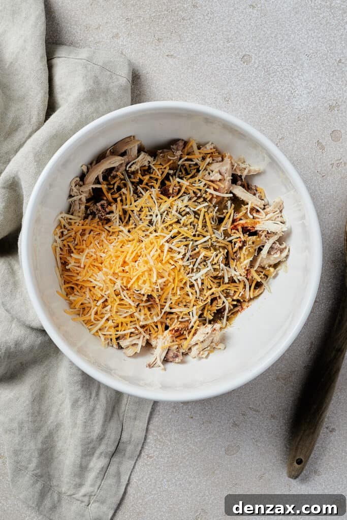 A white mixing bowl filled with the prepared chicken enchilada filling, showing shredded chicken, melted cheese, and spices blended together.