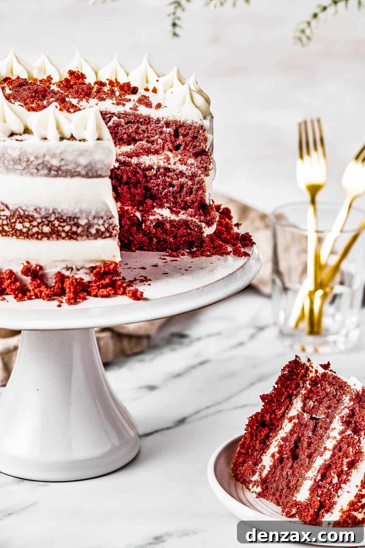 A cake on a cake stand, with a slice cut out and set on a small plate nearby.