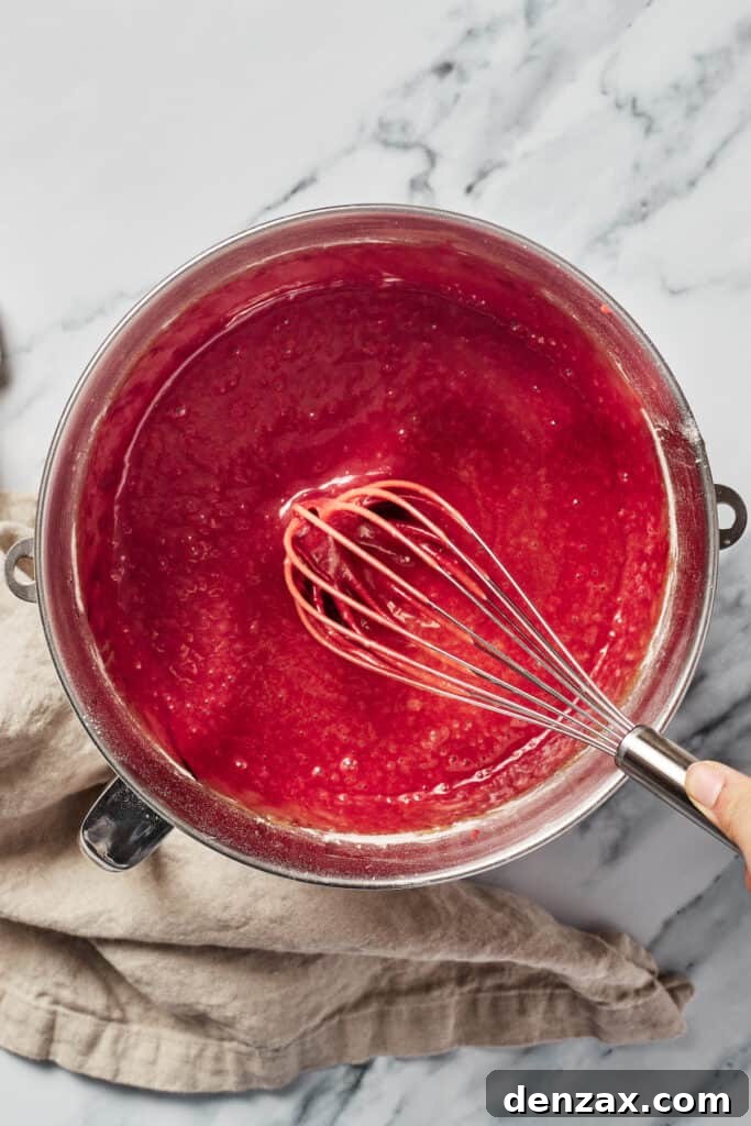 A mixing bowl of red cake batter with a whisk resting in it.
