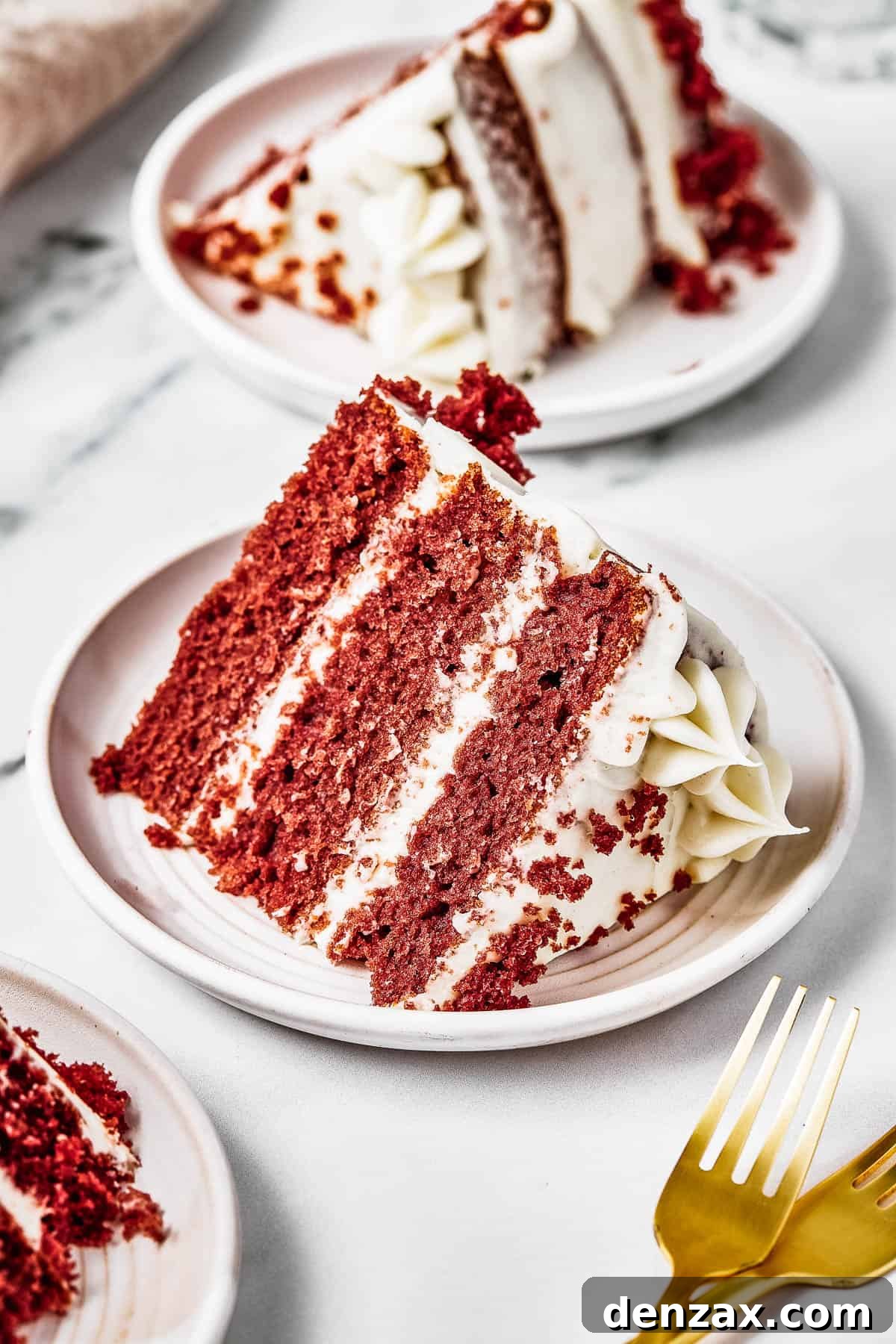 A slice of layer cake on a small plate, with golden forks next to it on the table.