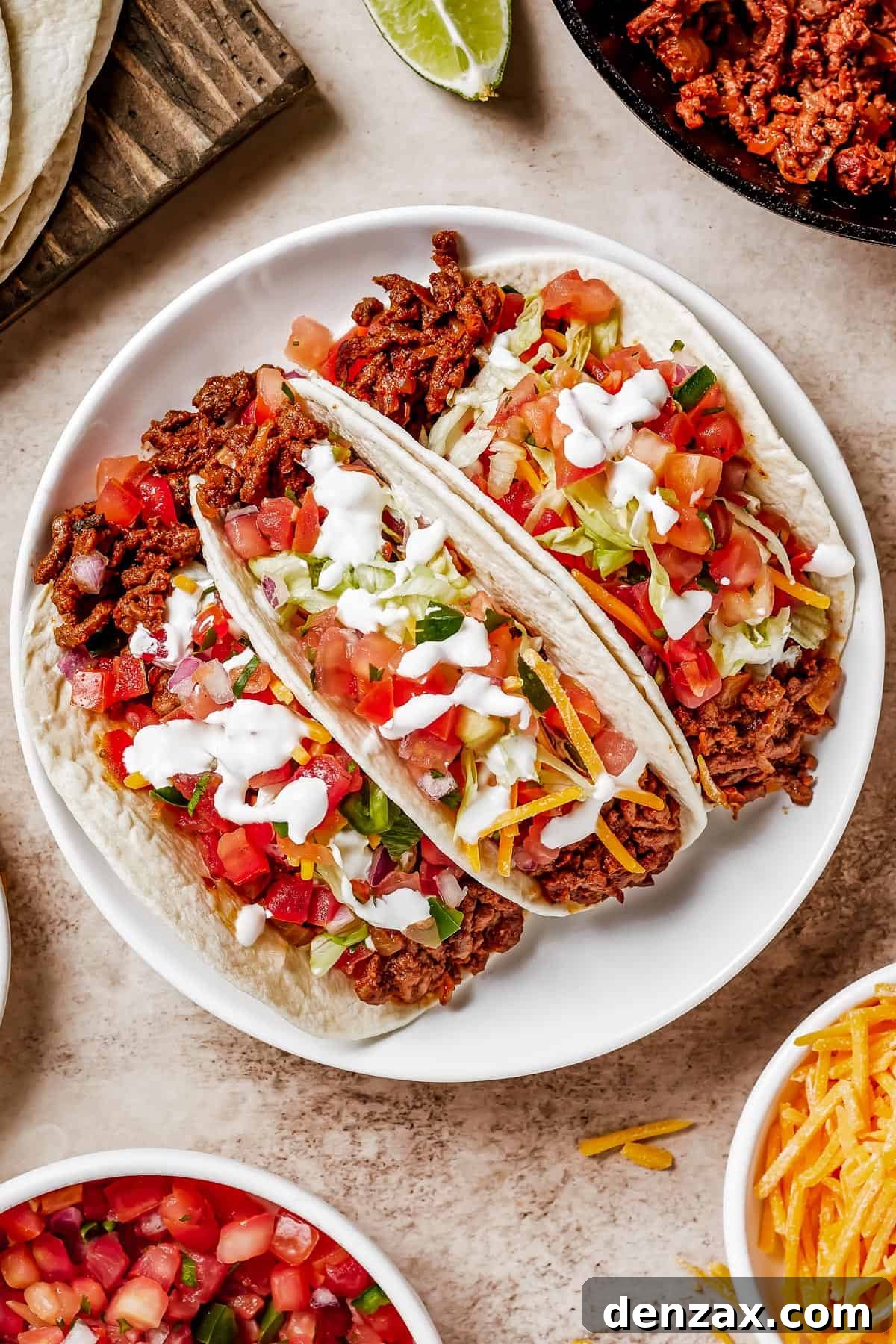Three soft tacos on a plate with fresh lime wedges, showcasing a vibrant and appealing meal.
