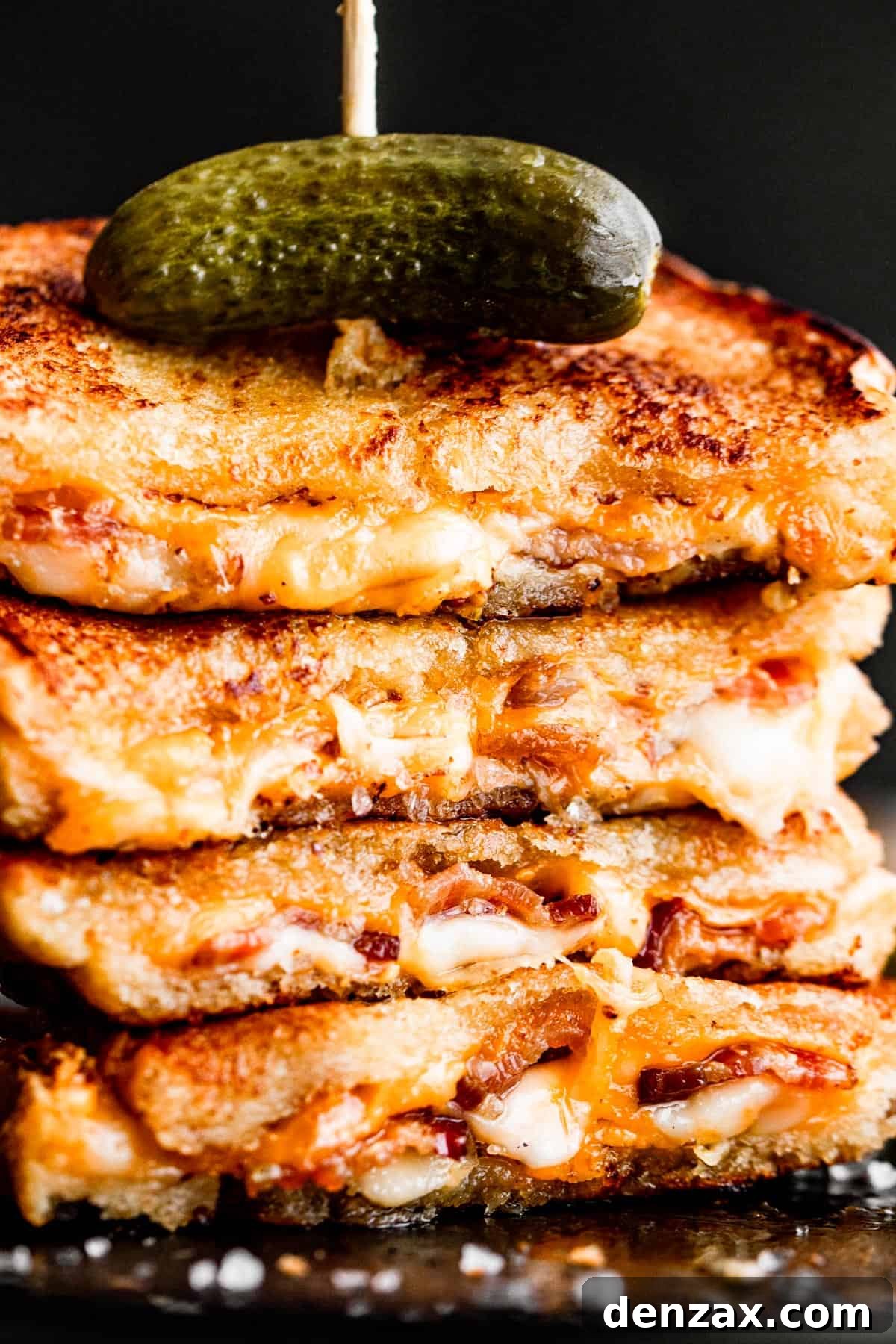 A stack of grilled cheese sandwiches topped with a pickle and a long toothpick, showcasing multiple servings.