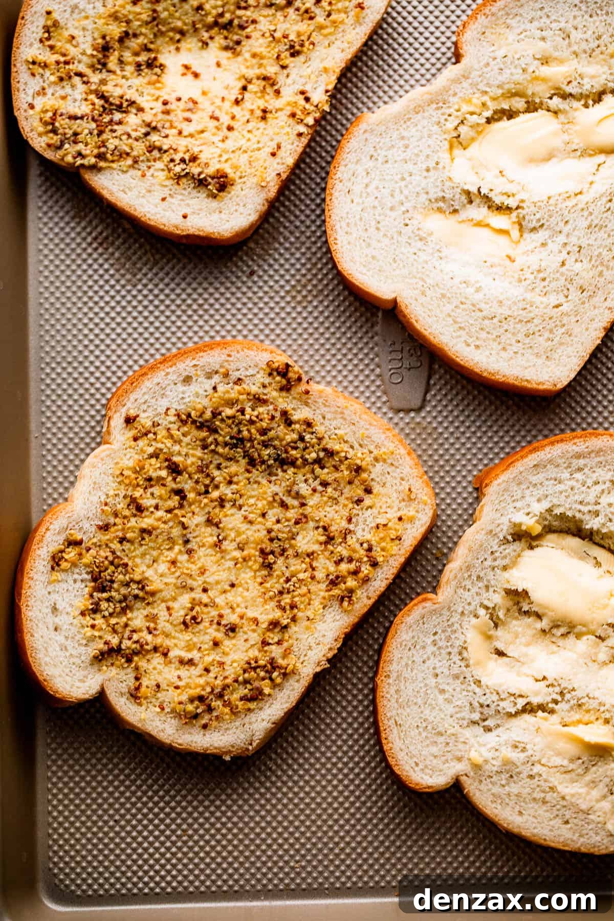 Four slices of bread generously topped with dijon mustard and mayonnaise, ready for cheese.