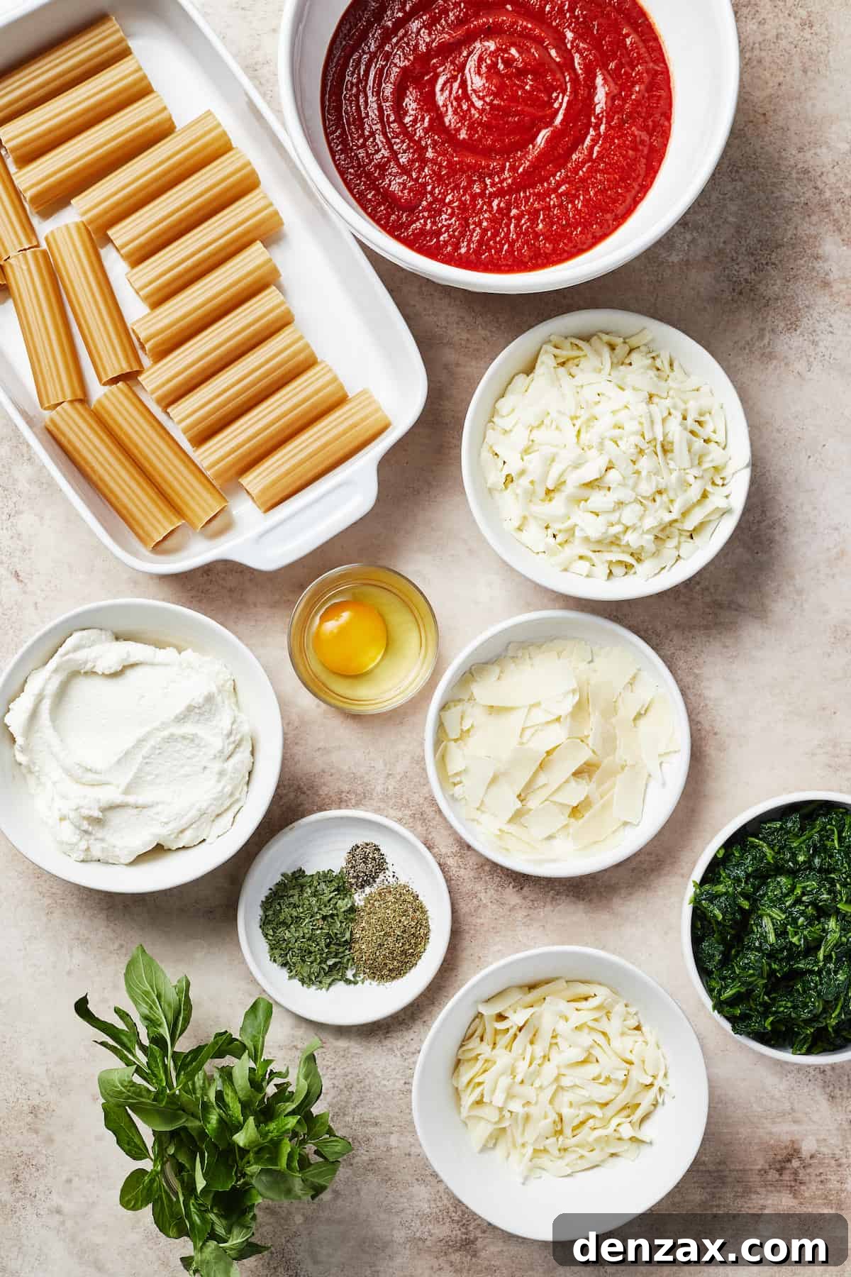 From top left: Uncooked manicotti pasta, vibrant marinara sauce, shredded mozzarella, shredded provolone, fresh spinach, grated parmesan, a selection of aromatic spices, creamy ricotta cheese, and a fresh egg – all essential ingredients for a perfect manicotti.