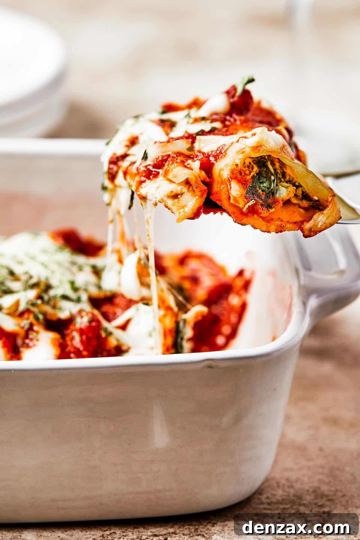 A serving of cheese manicotti being gently lifted from a casserole dish with a spatula, revealing its rich, melted cheese and sauce.