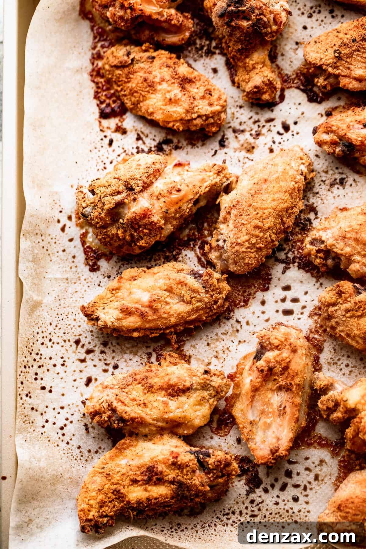 Cooked hot wings, perfectly crispy and golden-brown, arranged on a parchment-lined baking sheet after coming out of the oven.