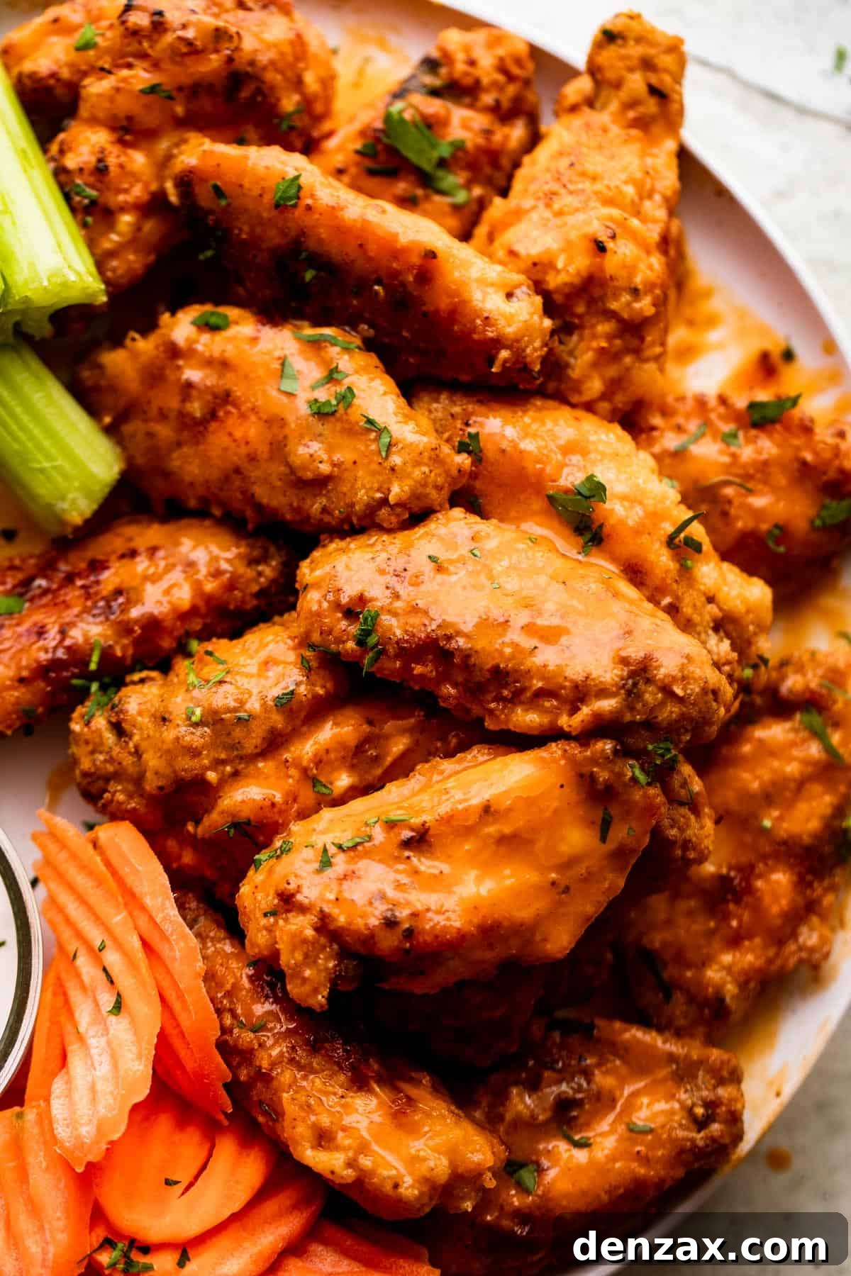 Close-up overhead shot of glistening Mango Habanero Hot Wings meticulously arranged on a pristine white serving plate, flanked by refreshing celery and carrot sticks.
