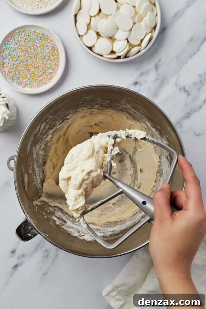 Smooth, creamy frosting in a mixing bowl, with a stand mixer attachment lifting out.