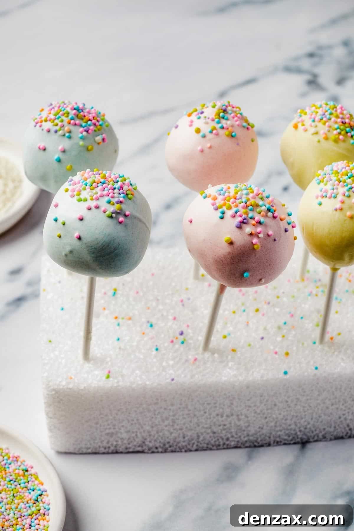 Lollipop cake pops with colorful sprinkles, meticulously drying upright in a styrofoam block.