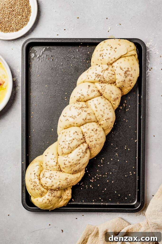 Unbaked egg bread on a sheet pan, being brushed with egg wash and sprinkled with sesame seeds.