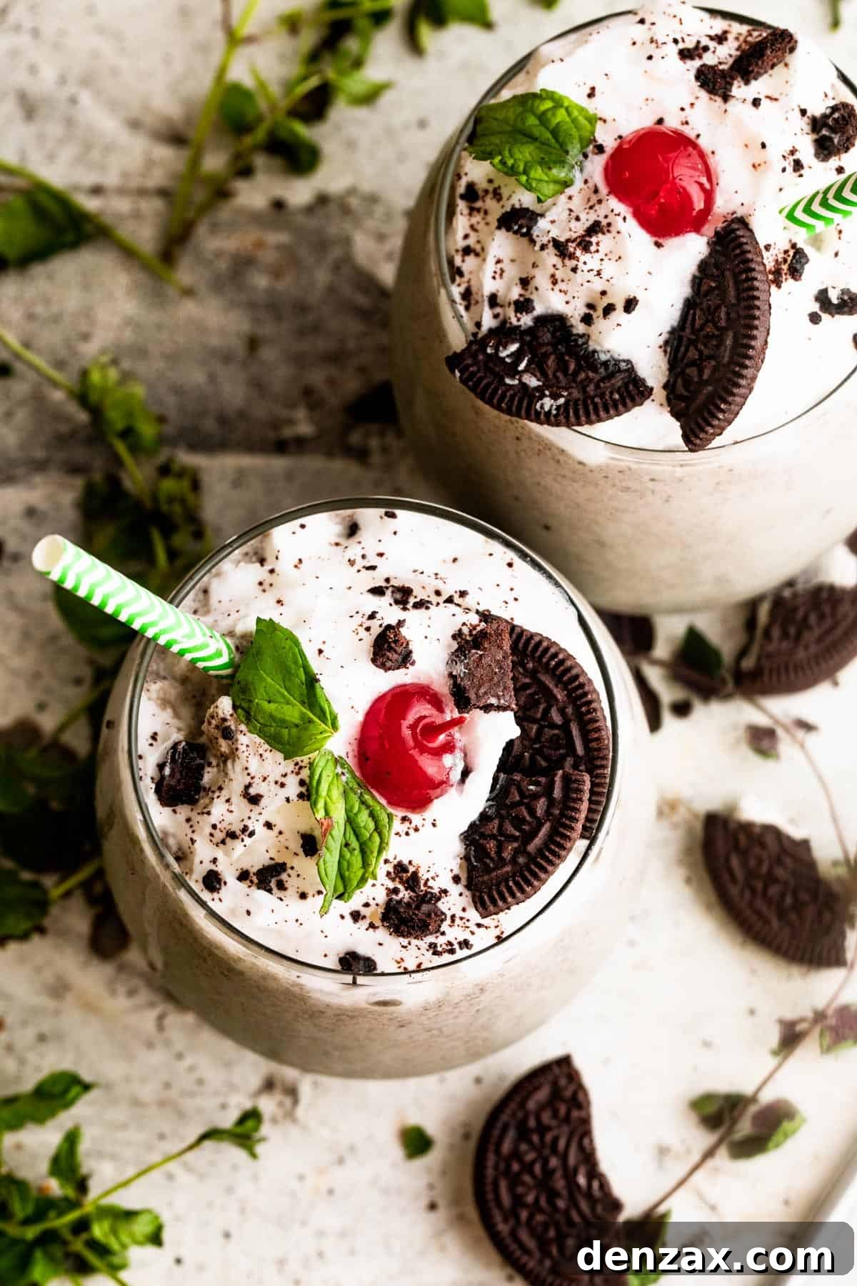 two drinking glasses filled with Shamrock Oreo McFlurry Shake, topped with whipped cream, maraschino cherries, and mint leaves.