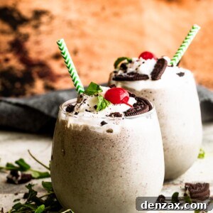 two drinking glasses filled with Shamrock Oreo McFlurry Shake, topped with whipped cream, maraschino cherries, and mint leaves.