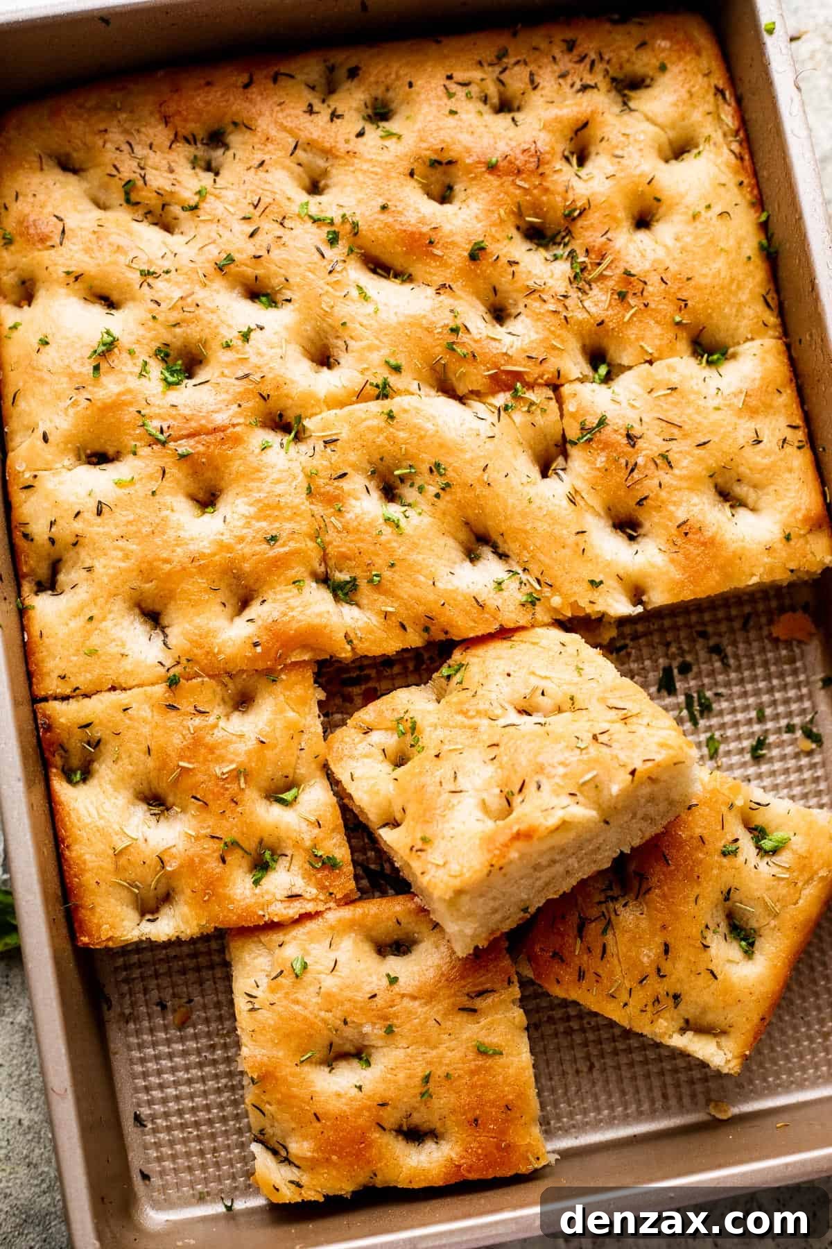 A large pan-sized loaf of focaccia, with four squares of bread cut away, revealing its airy interior.