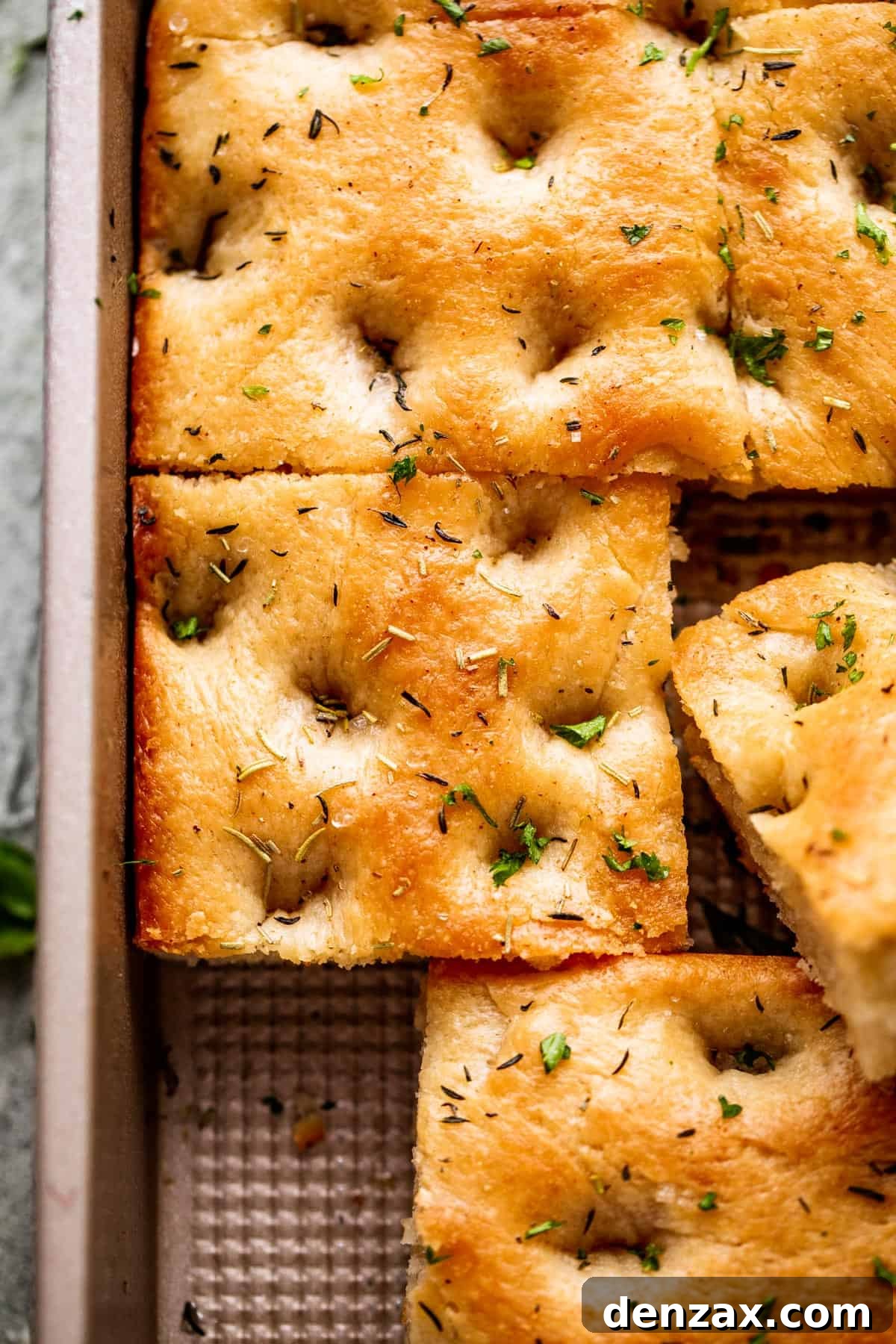 A large pan-sized loaf of focaccia, with one corner sliced away, ready to be served.