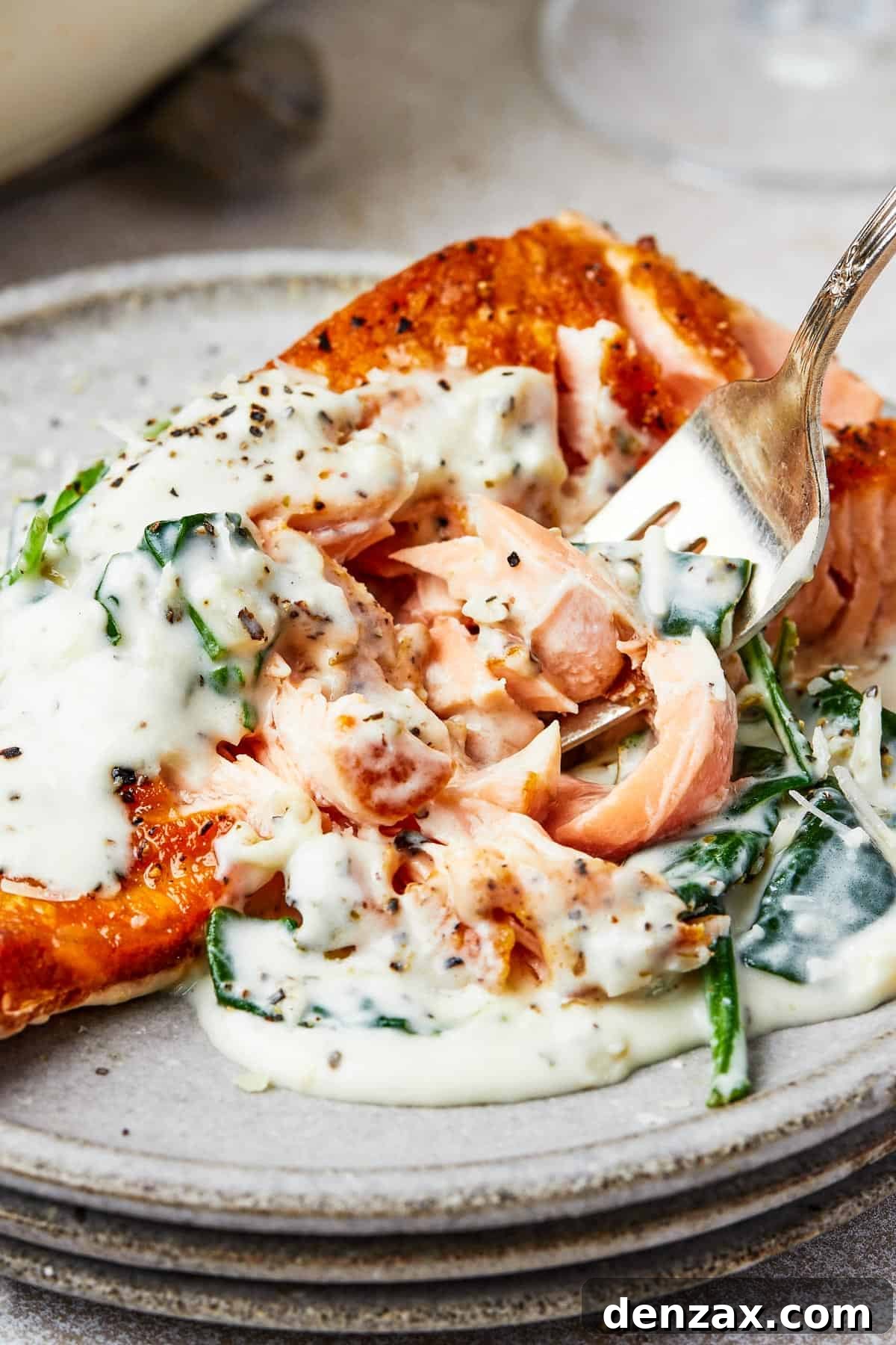 Creamy Florentine Salmon 2 A serving of salmon florentine. A bite of the salmon is being lifted toward the camera on a fork.
