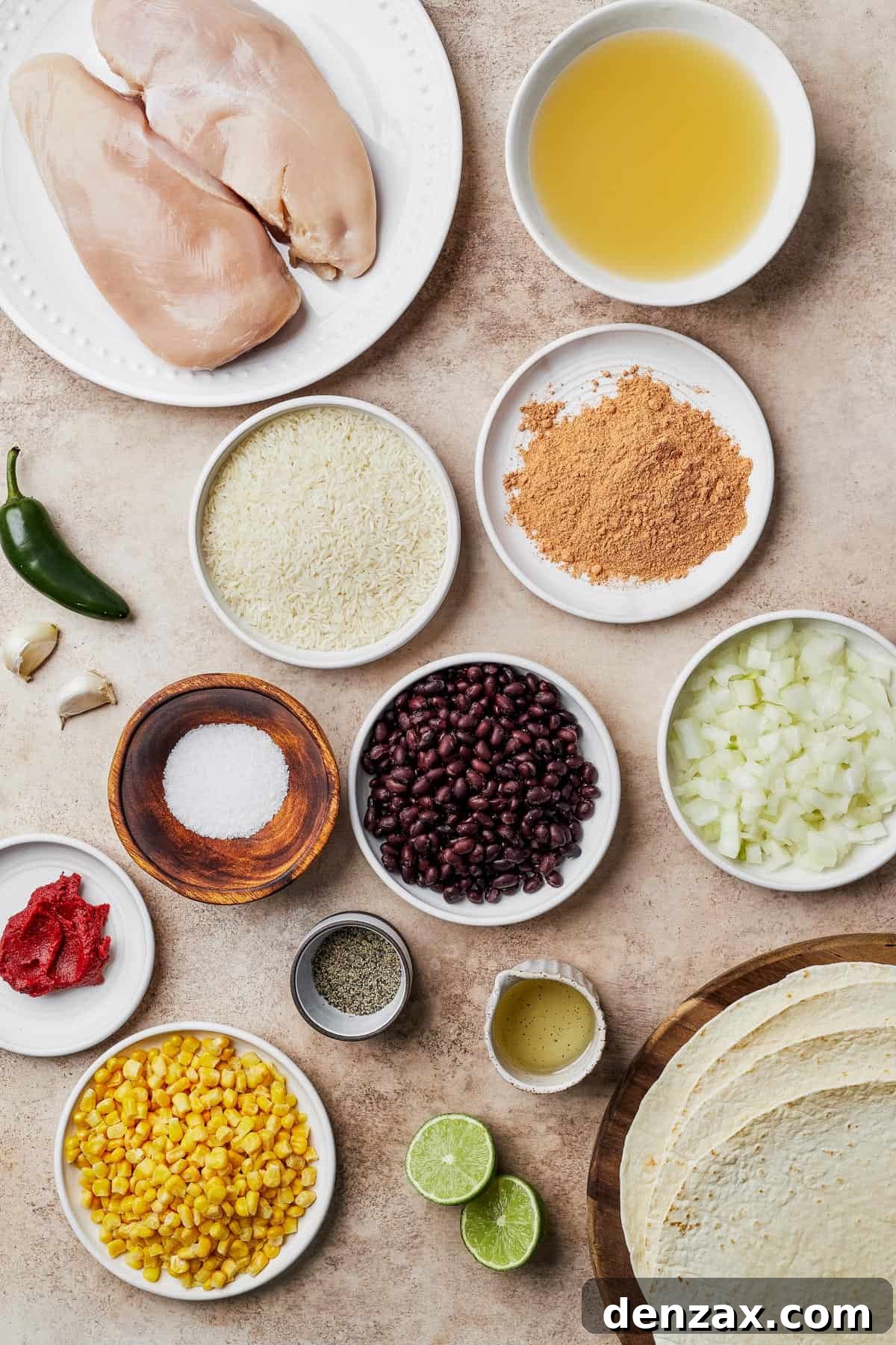 A vibrant flat lay of all ingredients for Instant Pot Chicken Burritos: raw chicken breasts, chicken broth, sliced jalapeño, minced garlic, white rice, taco seasoning, salt, black beans, chopped onions, tomato paste, pepper, corn kernels, fresh lime halves, and soft flour tortillas.
