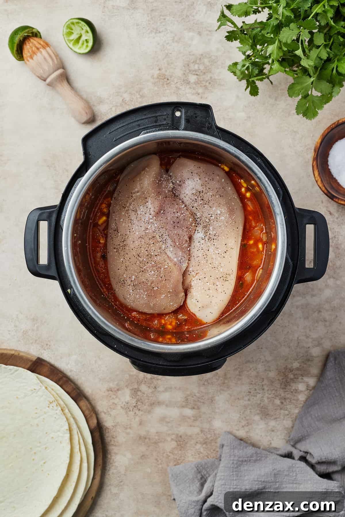 Uncooked boneless, skinless chicken breasts resting atop the colorful mixture of rice, beans, and vegetables inside an Instant Pot, seasoned and ready for pressure cooking.