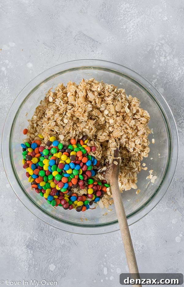 M&M Granola Bar mixture being firmly pressed into a parchment-lined baking pan