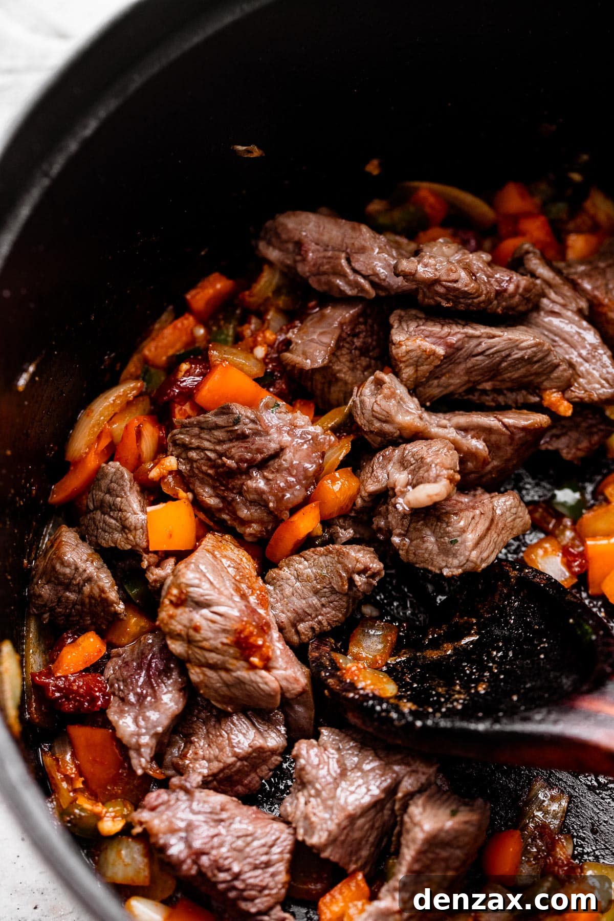 browning pieces of chuck roast and diced veggies inside a dark skillet.